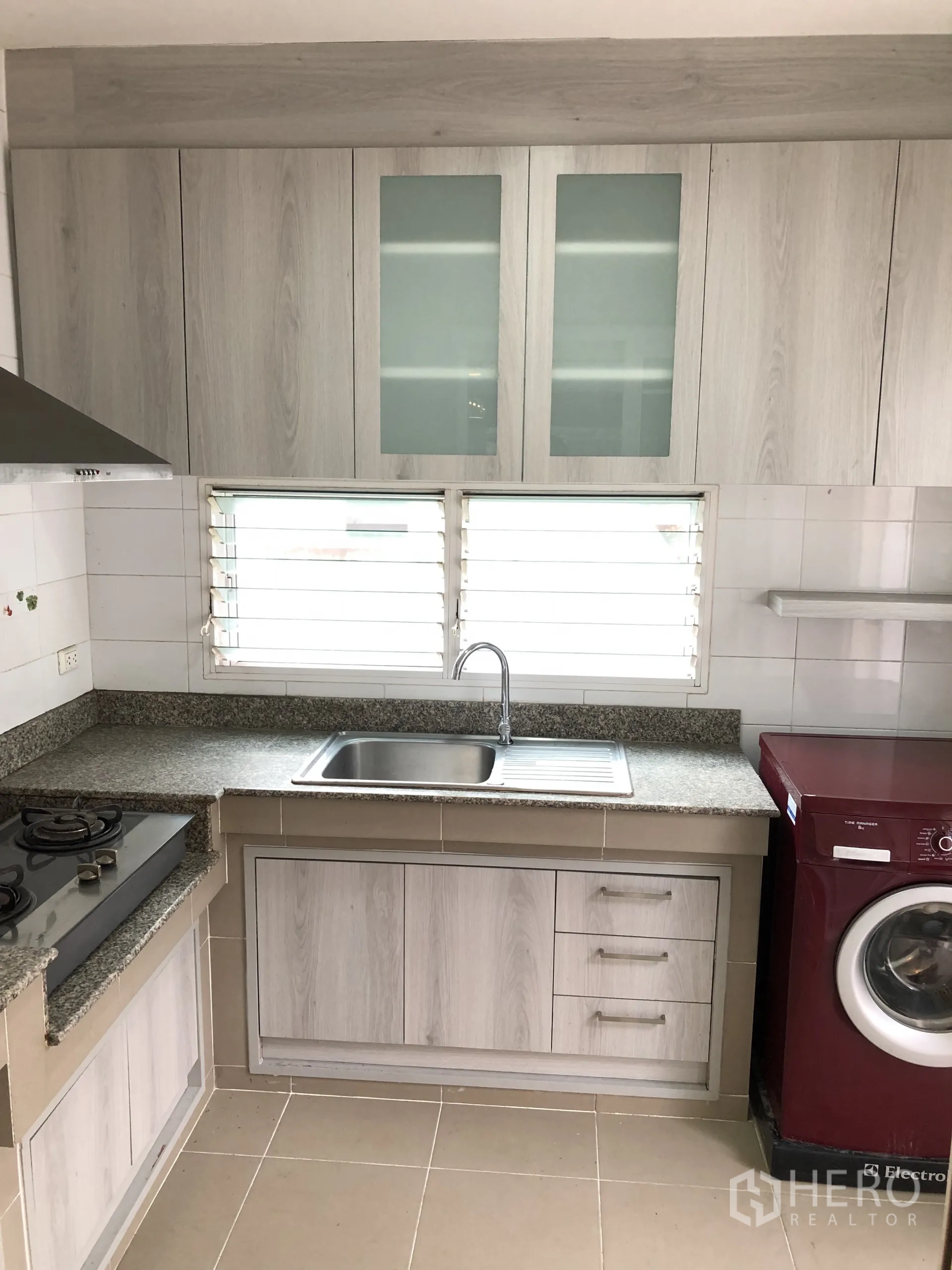 Detached House for rent in Bang Kapi, Bangkok - Kitchen cabinetry with sink under louvered window and a washing machine.