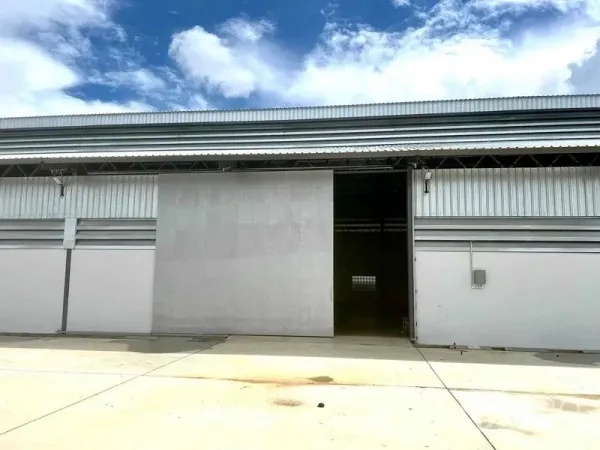Warehouse for rent in Mueang Samut Prakan, Samut Prakan - Front elevation of a modern warehouse with large sliding metal door and wide concrete apron under a blue sky.