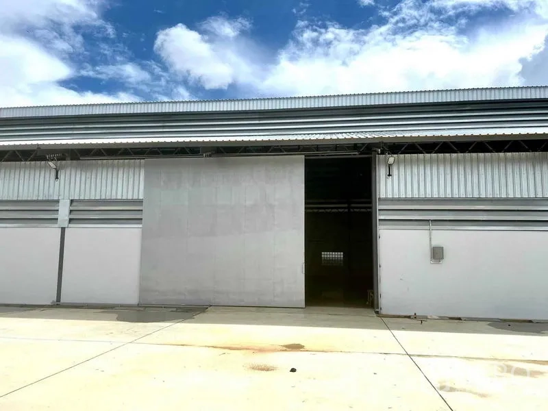 Warehouse for rent in Mueang Samut Prakan, Samut Prakan - Front elevation of a modern warehouse with large sliding metal door and wide concrete apron under a blue sky.