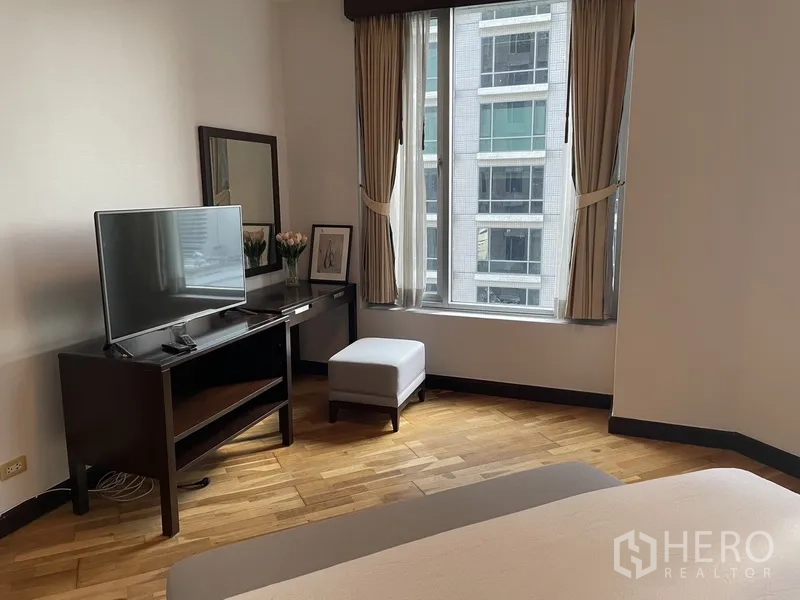 公寓 出租或出售在Pathum Wan, Bangkok - 卧室角落设电视柜、书桌与镜子，窗外可见邻近建筑。