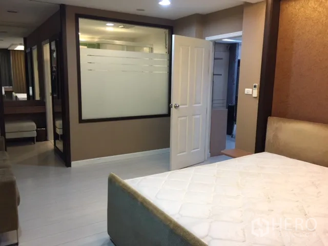 Condominium for rent or sale in Khlong Toei, Bangkok - Spacious bedroom with bed, frosted glass partition and doorway to ensuite.