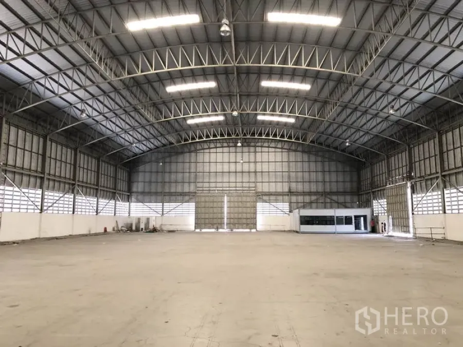 货栈 出租在Pathum Thani - 明亮开放的仓库大厅，钢结构屋架、卷帘门与内部办公室模块。
