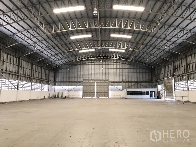 货栈 出租在Pathum Thani - 明亮开放的仓库大厅，钢结构屋架、卷帘门与内部办公室模块。