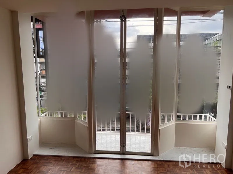 Shophouse for rent or sale in Watthana, Bangkok - Floor-to-ceiling frosted glass doors opening to a small balcony with urban outlook.