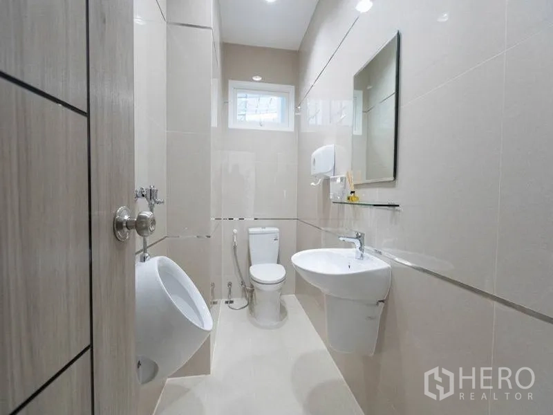 Factory for rent in Bang Bo, Samut Prakan - Clean tiled restroom with toilet, urinal, sink, mirror and a small window for ventilation.