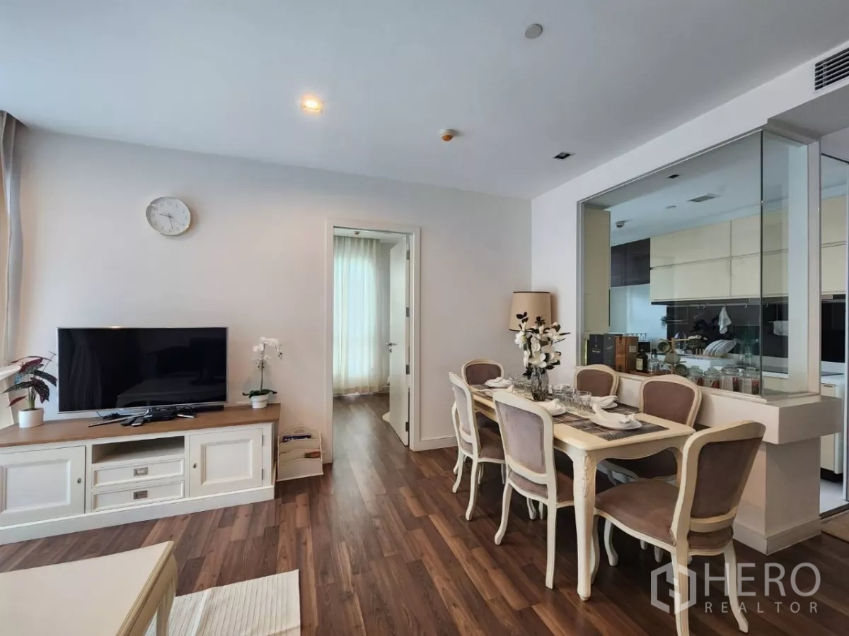Condominium for rent in Phra Khanong, Bangkok - View of dining table and TV area with doorway to a bedroom and mirrored wall.