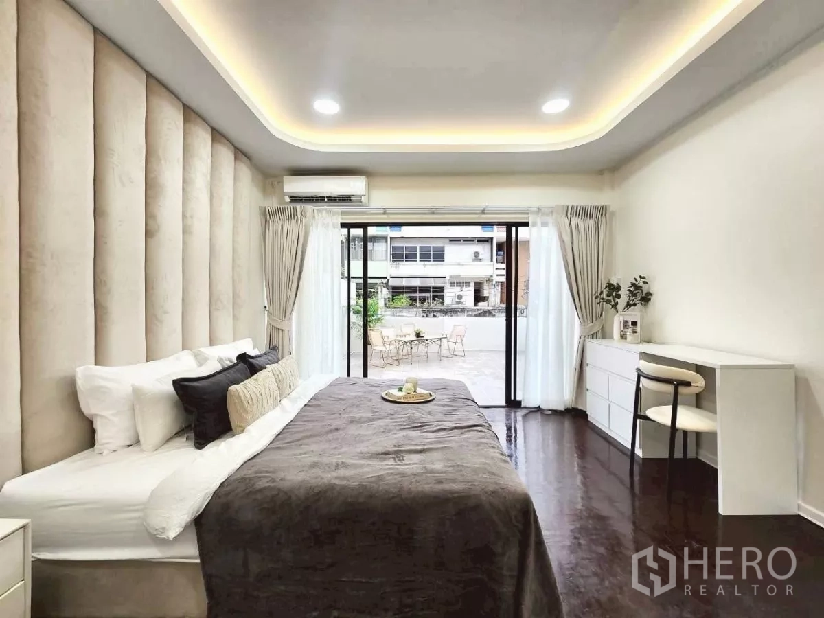 Townhouse for rent in Huai Khwang, Bangkok - Bedroom opening to a spacious terrace through sliding glass doors with desk and drawers.