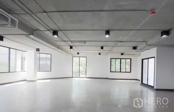 办公空间 出租在Watthana, Bangkok - 角落办公室，环绕窗带来自然采光，光滑水泥地与现代吊顶灯具。