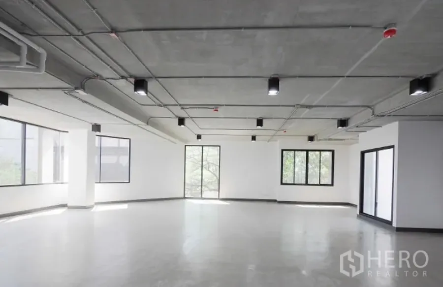 办公空间 出租在Watthana, Bangkok - 角落办公室，环绕窗带来自然采光，光滑水泥地与现代吊顶灯具。