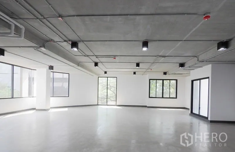办公空间 出租在Watthana, Bangkok - 角落办公室，环绕窗带来自然采光，光滑水泥地与现代吊顶灯具。