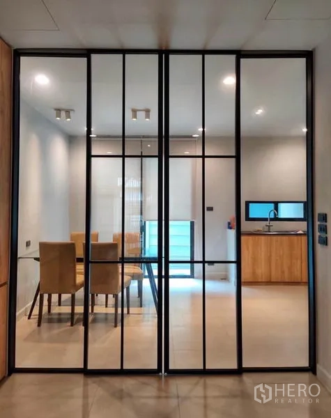 Townhouse for rent in Suan Luang, Bangkok - Black-framed glass partition opening to the dining room and light-wood kitchen