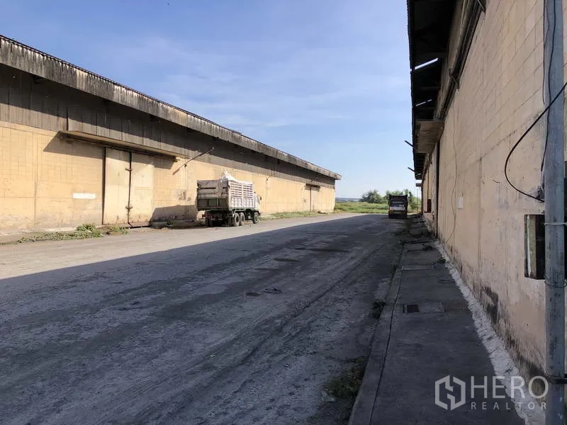 Warehouse for rent in Phra Nakhon Si Ayutthaya - Service road along warehouse row with trucks and loading bays facing open fields.