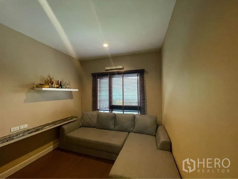 Detached House for rent or sale in Bang Phli, Samut Prakan - Cozy media room with an L-shaped gray sofa, window blinds and a floating wall shelf.