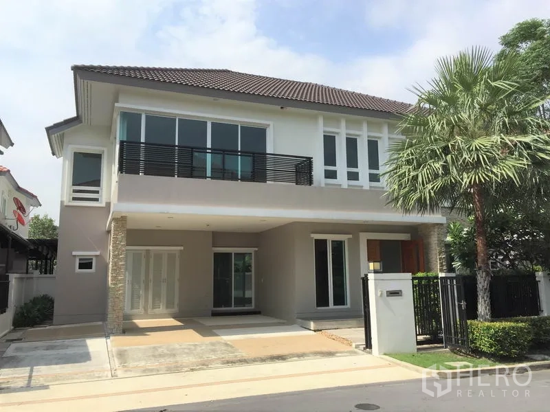 Detached House for rent in Saphan Sung, Bangkok - Modern two-storey detached house with balcony, tiled roof, gated entrance and driveway shaded by a palm tree.