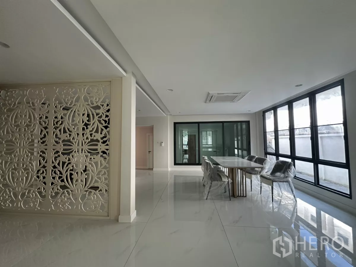 Townhouse for rent in Watthana, Bangkok - Open-plan dining area with long table, floor-to-ceiling windows, and a decorative lattice partition.