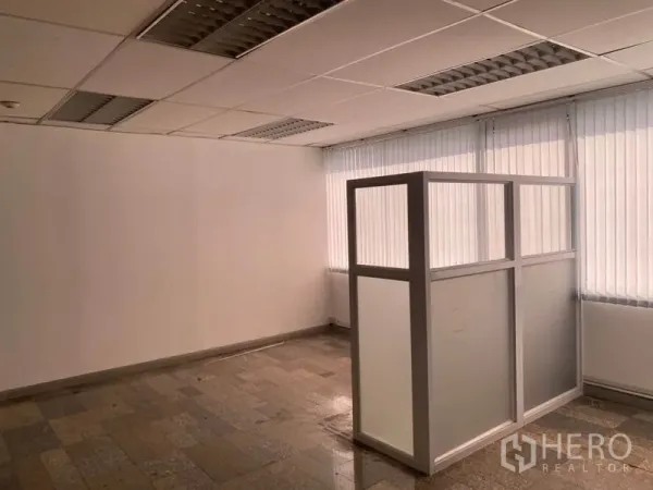 Office Space for rent in Khlong Toei, Bangkok - Corner office interior with vertical blinds, suspended ceiling lights and a frosted glass partition on stone-tile flooring.