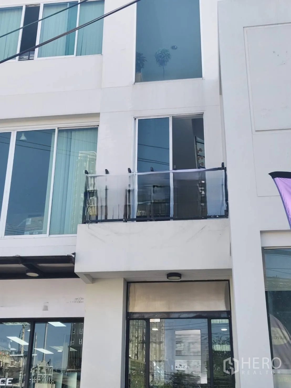 Home Office for rent in Bang Kapi, Bangkok - Modern white home office building with full-height glass storefront, sliding windows, and a small balcony with tinted railing on a city street in Bangkok.