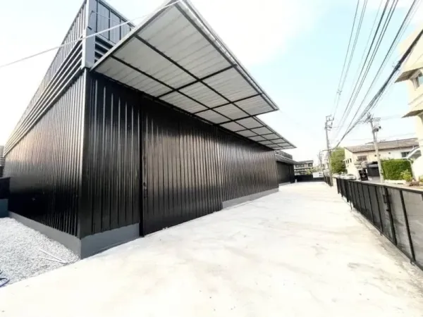 Warehouse for rent in Lat Phrao, Bangkok - Modern black metal warehouse exterior in Lat Phrao with covered loading canopy and a wide concrete driveway.