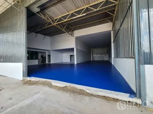 Factory for rent in Lam Luk Ka, Pathum Thani - High-clearance factory bay with blue epoxy floor, steel truss roof and wide loading entrance.