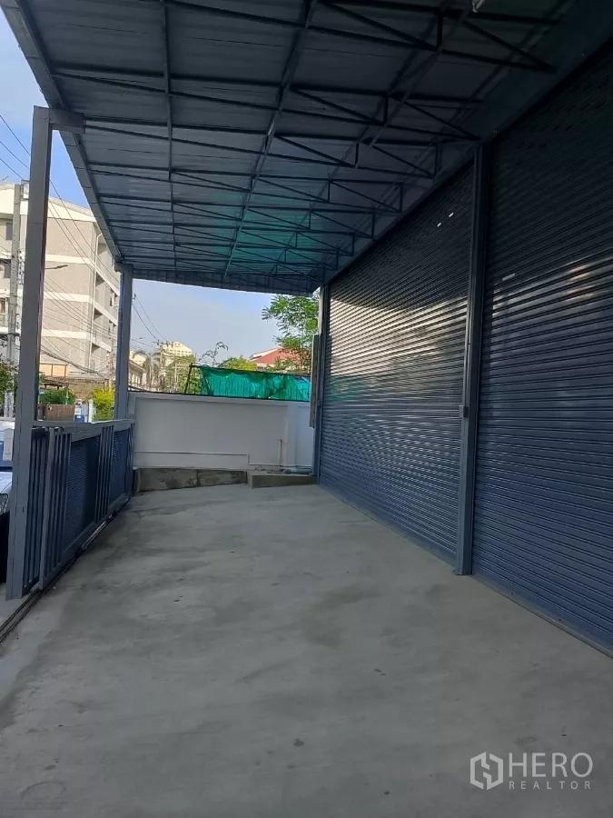 货栈 出租在Huai Khwang, Bangkok - 屋檐下的侧向车道与装卸区，旁为灰色卷闸门。