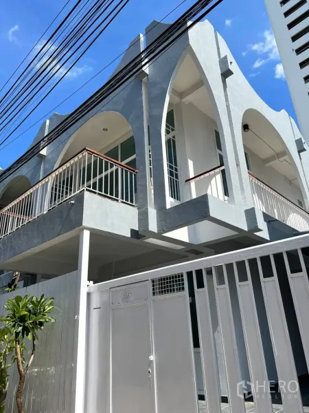 带办公室的家 出租在Watthana, Bangkok - 两层办公住宅外观，拱形阳台与金属大门，天空晴朗。