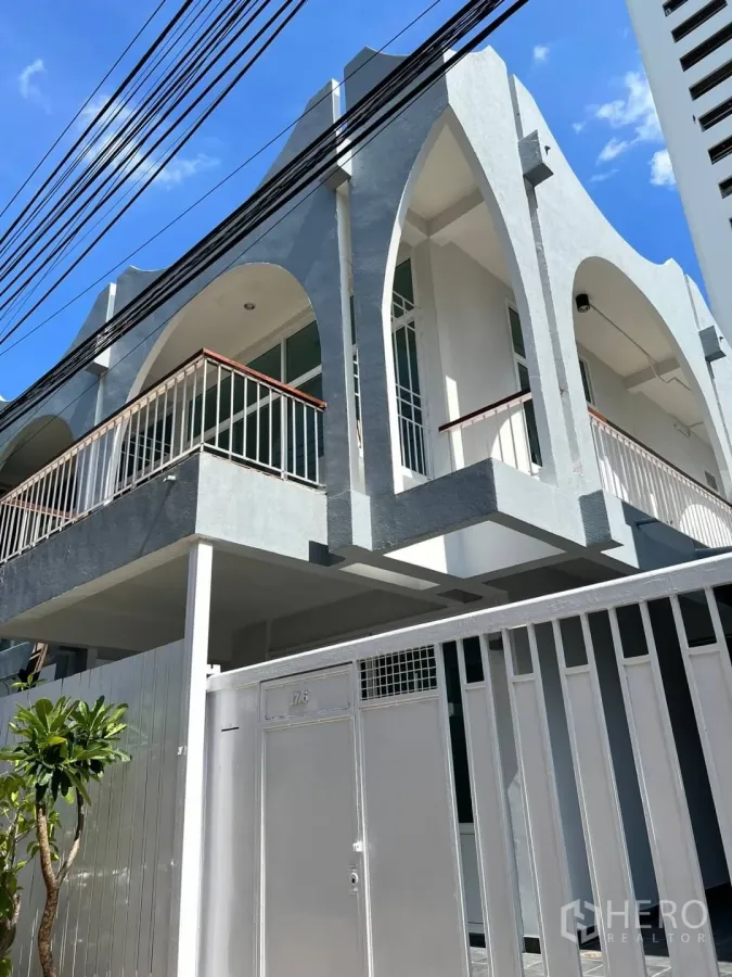 带办公室的家 出租在Watthana, Bangkok - 两层办公住宅外观，拱形阳台与金属大门，天空晴朗。