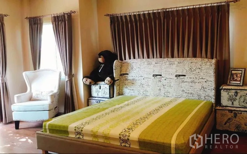 Detached House for rent or sale in Bang Yai, Nonthaburi - Warm bedroom with large upholstered bed, armchair and full-height windows with curtains.