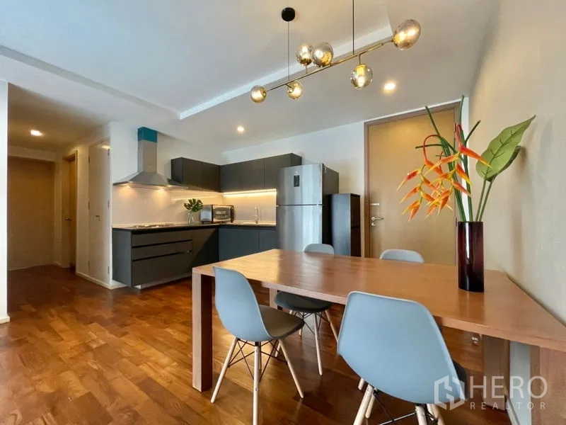 Condominium for rent or sale in Khlong Toei, Bangkok - Dining table for four under pendant lights next to sleek grey kitchen.