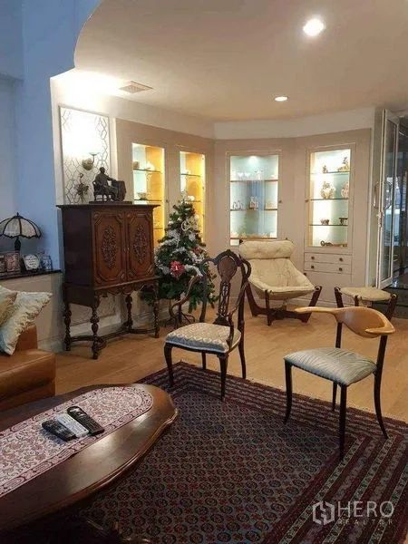 Townhouse for sale in Yan Nawa, Bangkok - Elegant living room with illuminated display shelves, antique cabinet, lounge chairs and rug.