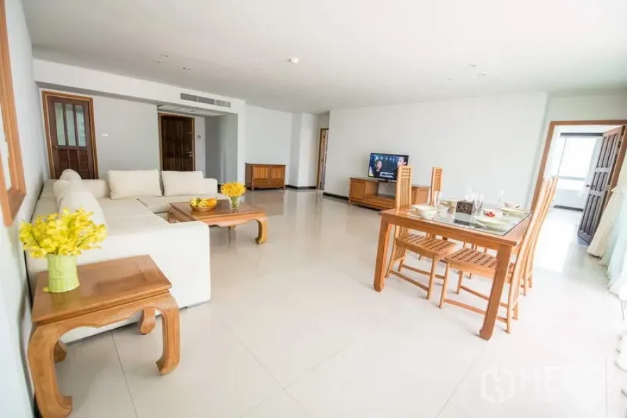 Apartment for rent in Sathon, Bangkok - Bright open-plan living and dining room with white sofa, wooden furniture and TV.