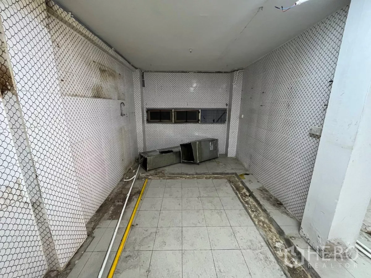 Shophouse for rent in Watthana, Bangkok - Ground-floor tiled space with mesh-lined walls and small horizontal windows.