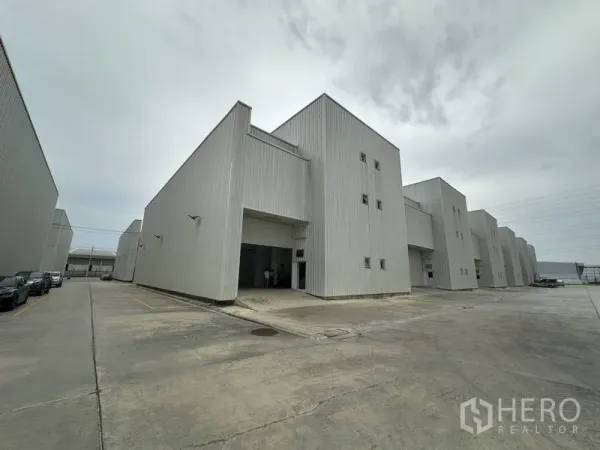 Factory for rent in Khlong Luang, Pathum Thani - Row of modern light-grey factory units with wide concrete driveway for truck access.