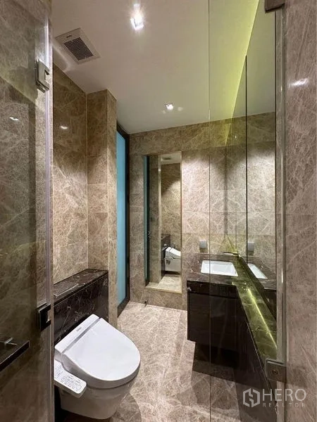 Condominium for rent in Pathum Wan, Bangkok - Luxurious marble bathroom with large mirrors, vanity cabinet and smart toilet.