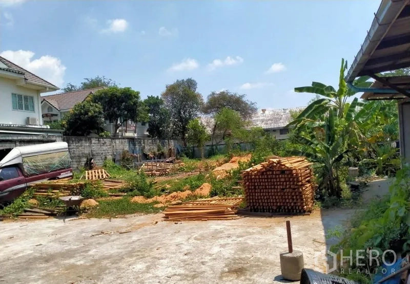 Warehouse for sale in Mueang Nonthaburi, Nonthaburi - Open back lot with lumber piles, greenery and neighboring houses.