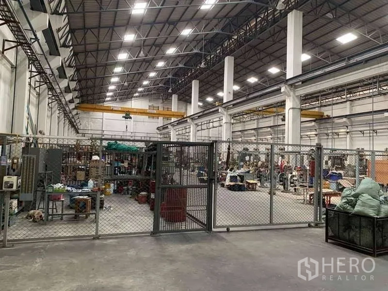 Factory for rent in Phra Samut Chedi, Samut Prakan - Large industrial hall with chain‑link safety fence, high roof and overhead bridge cranes.