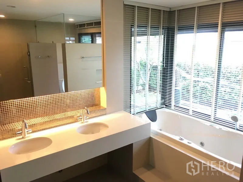 Detached House for rent or sale in Bang Kapi, Bangkok - Master bathroom with double vanity and corner bathtub beside wide windows.