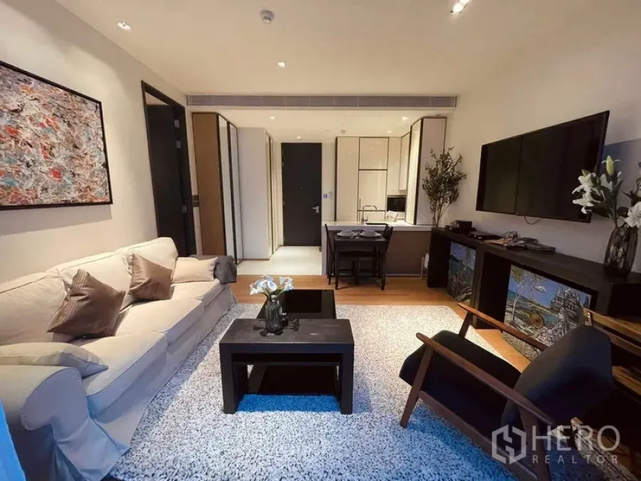 Condominium for rent in Khlong Toei, Bangkok - Contemporary living room with sofa, TV wall, coffee table, rug and adjacent dining area.
