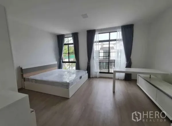 Townhouse for rent in Bang Phli, Samut Prakan - Spacious bedroom with floor-to-ceiling windows, sheer curtains, bed and work desk.