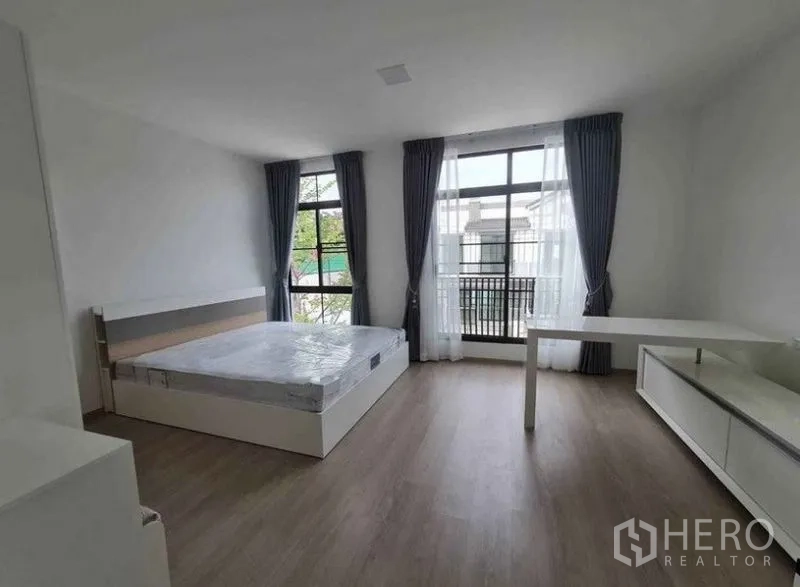 Townhouse for rent in Bang Phli, Samut Prakan - Spacious bedroom with floor-to-ceiling windows, sheer curtains, bed and work desk.
