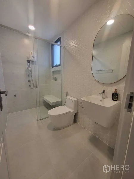 Detached House for rent in Saphan Sung, Bangkok - Minimalist white bathroom with glass shower enclosure and wall-hung sink.