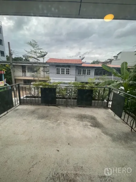 Detached House for rent in Watthana, Bangkok - Spacious balcony with metal railing overlooking neighborhood houses under a cloudy sky.