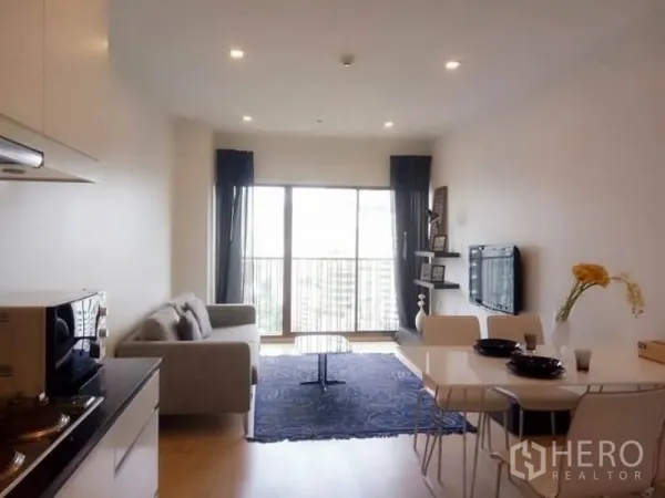 Condominium for rent in Bangkok - Bright living and dining area with sofa, balcony doors and wall‑mounted TV in a city condo.