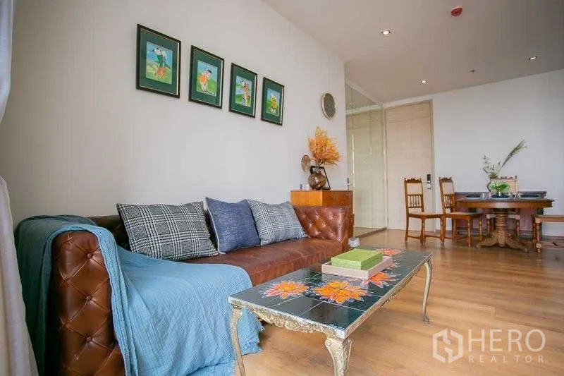 Condominium for sale in Khlong Toei, Bangkok - Leather sofa with cushions and a decorative glass coffee table in a bright lounge.