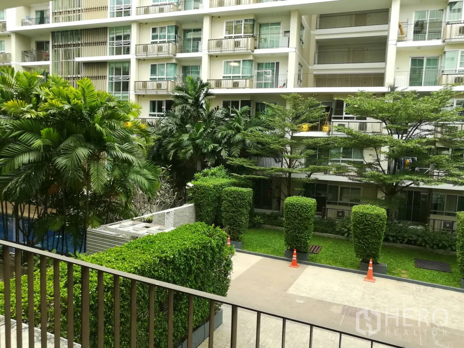 Condominium for rent in Watthana, Bangkok - View from the balcony over a landscaped courtyard with trimmed hedges, palm trees and pool.