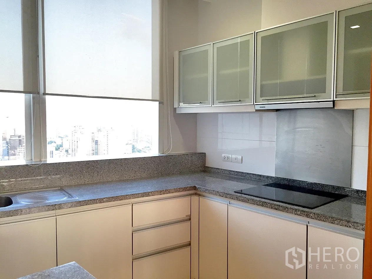Condominium for rent in Khlong Toei, Bangkok - Separate L-shaped kitchen with granite countertops, electric cooktop, extractor and large window.