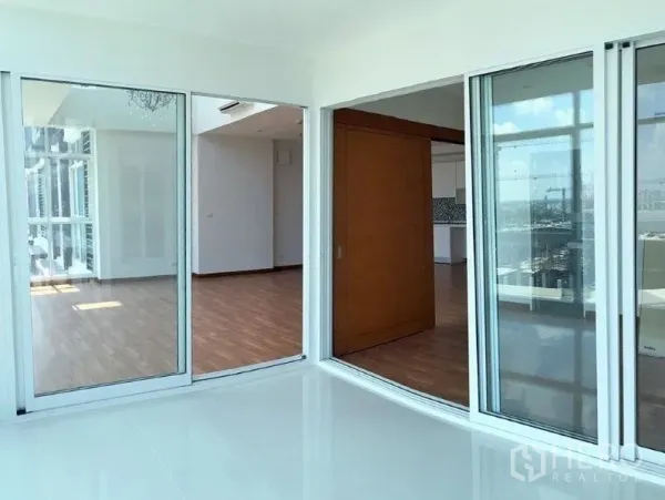 Condominium for sale in Bang Na, Bangkok - Sunlit room with sliding glass doors opening to the adjacent living area and balcony.