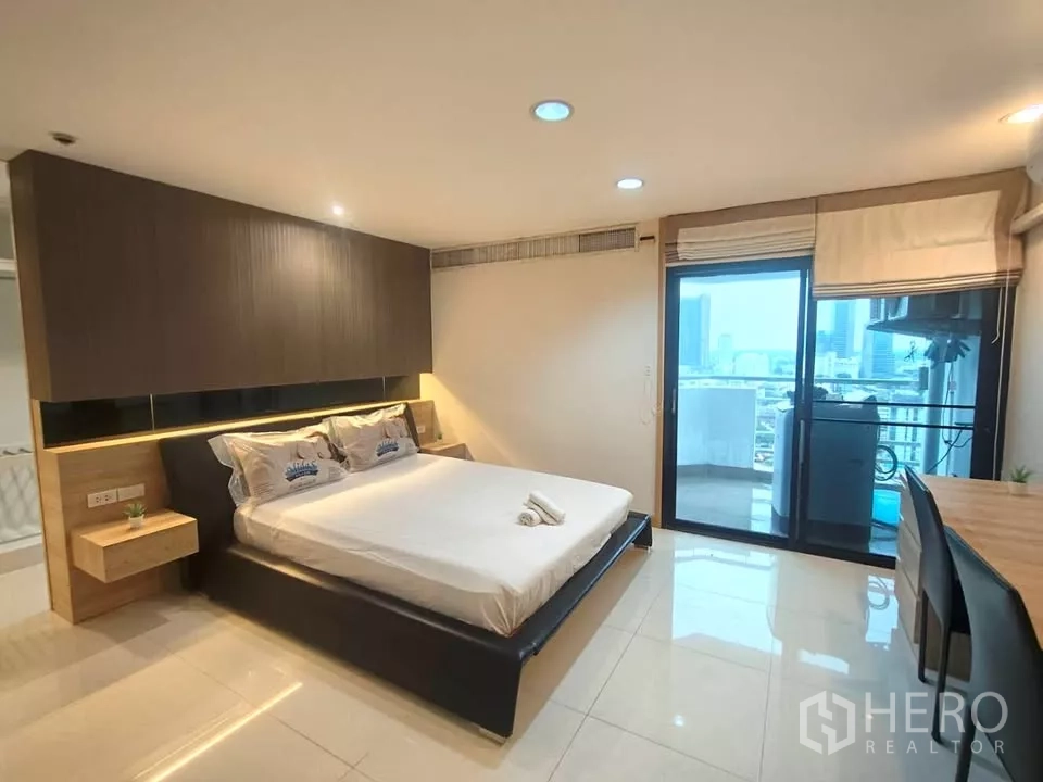 Condominium for rent in Khlong Toei, Bangkok - Primary bedroom with king bed and sliding doors opening to a city-view balcony.
