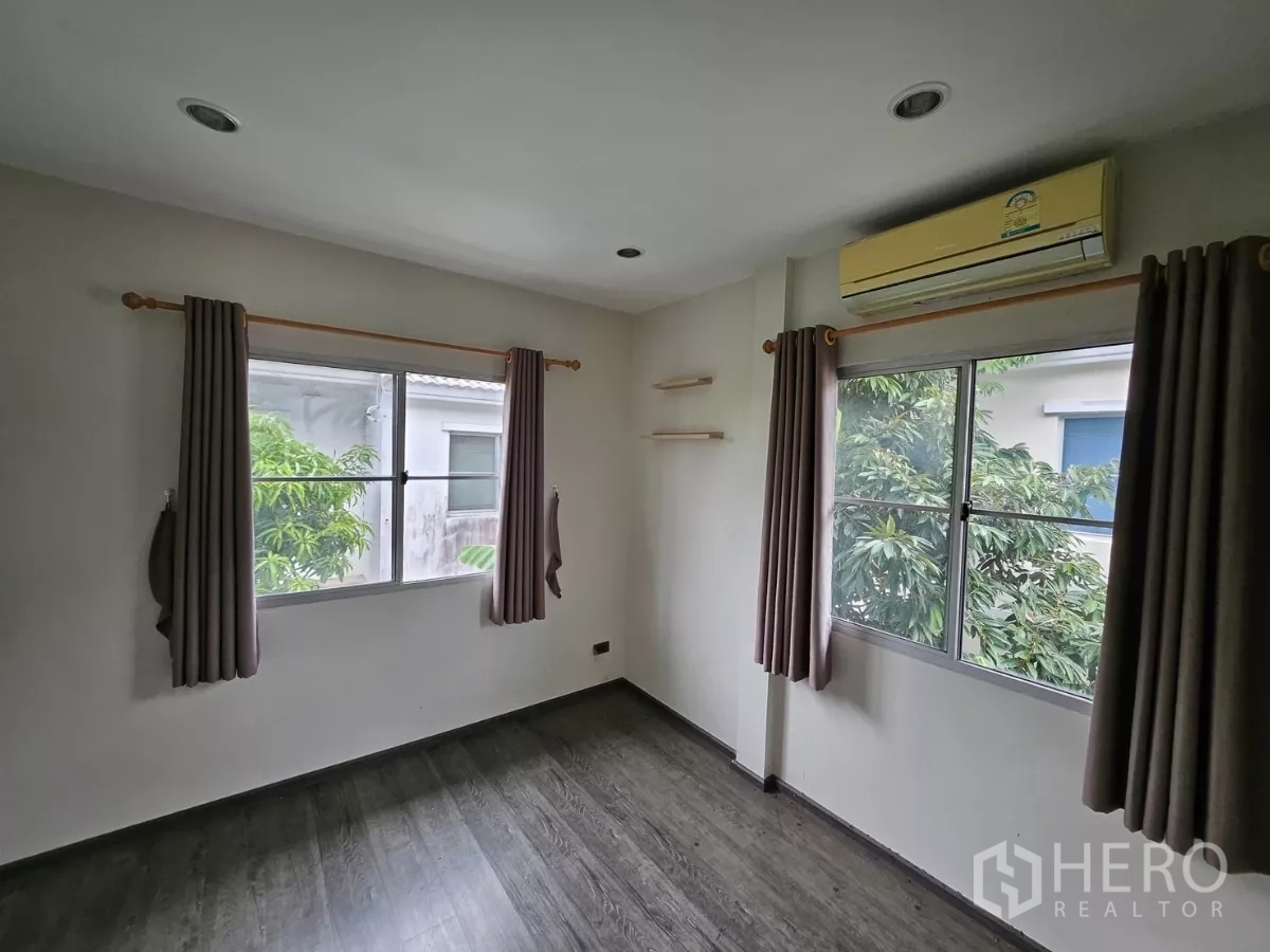 Detached House for rent in Khlong Toei, Bangkok - Secondary bedroom with two windows, air conditioner and wood-look flooring.