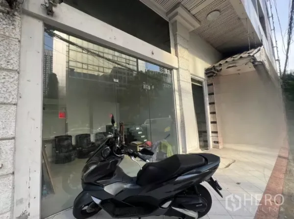 Retail Space for rent - Angled view of glass-front retail entrance with scooter parked along the tiled walkway.