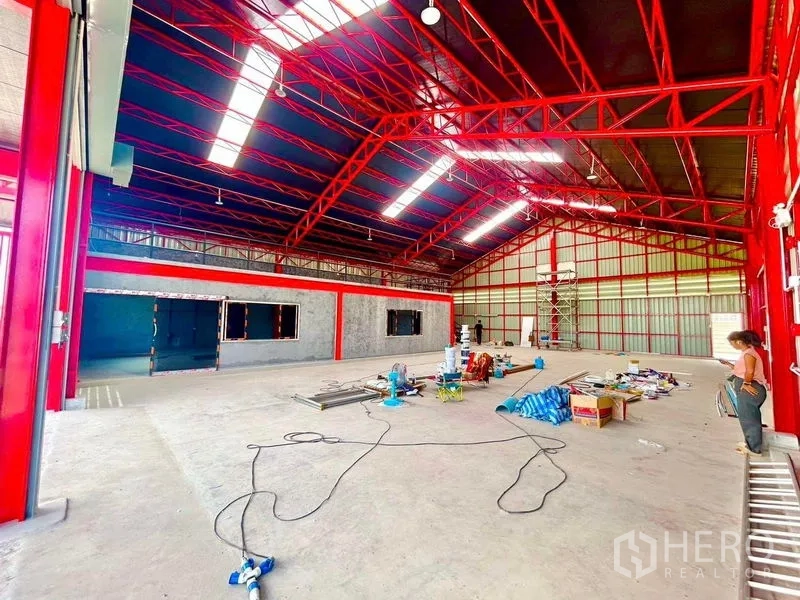 Warehouse for rent in Lam Luk Ka, Pathum Thani - Large column-free warehouse interior with a red steel frame and work materials on the floor.